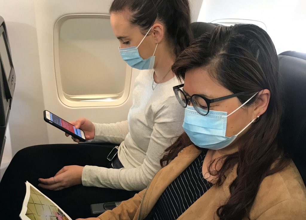 two women wearing face masks and looking at a phone