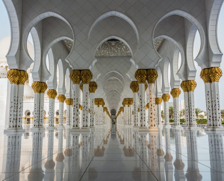 a large white and gold building with columns with Sheikh Zayed Mosque in the background