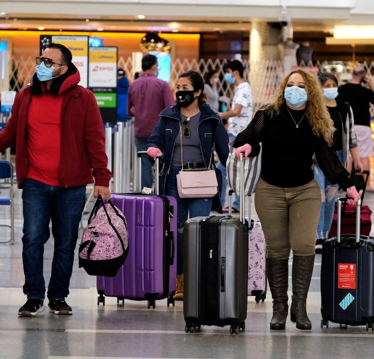 a group of people wearing face masks walking with luggage