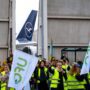 a group of people in yellow vests holding signs and a plane in the background