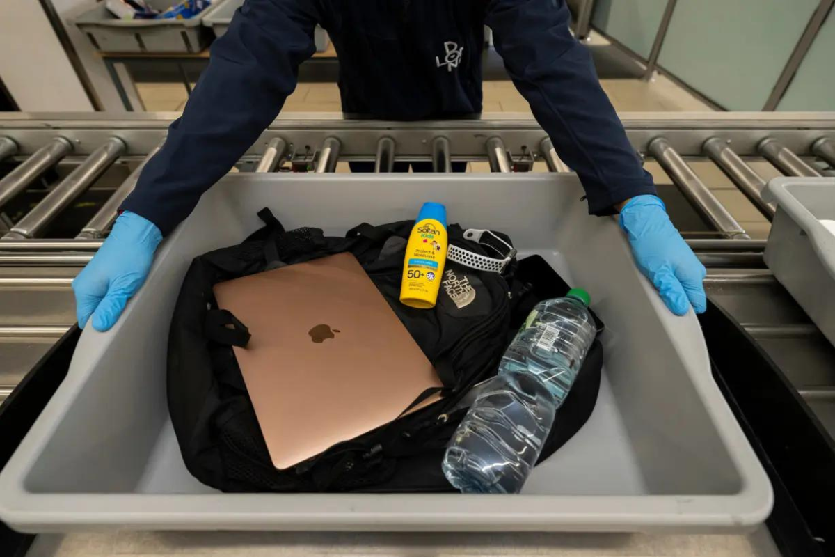 a person holding a tray with a laptop and a bottle of sunblock