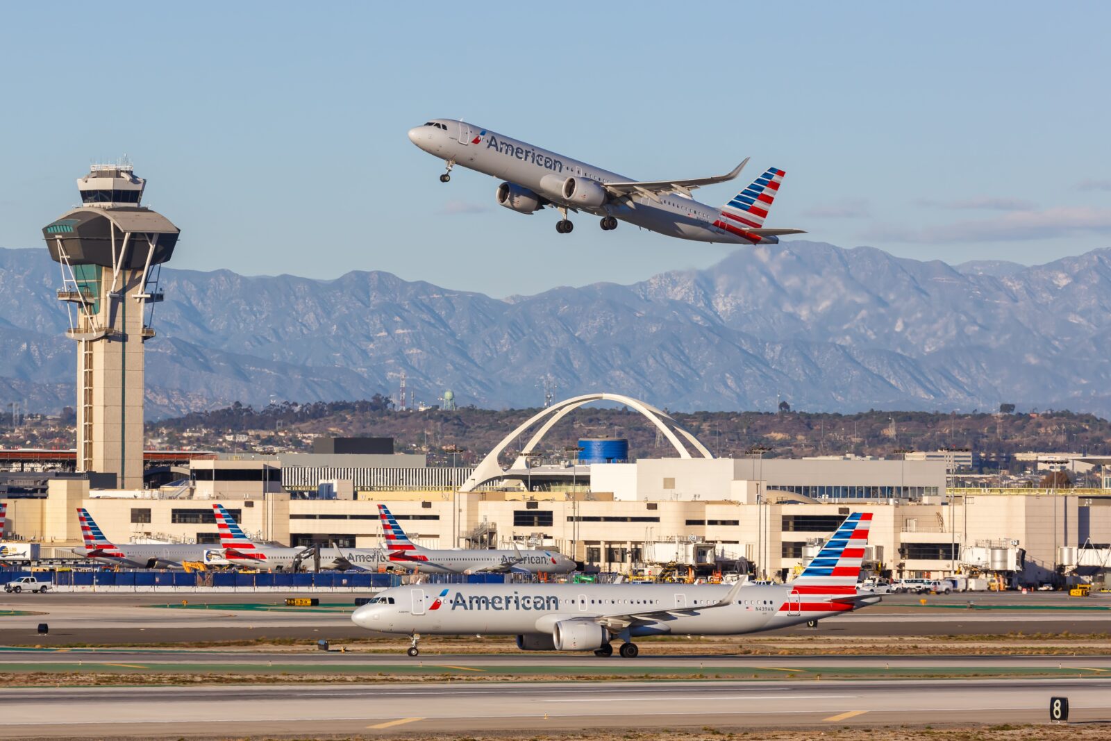 an airplane flying over a runway with buildings and mountains in the background