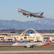 an airplane flying over a runway with buildings and mountains in the background