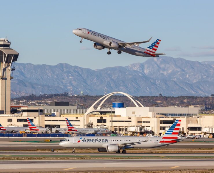 an airplane flying over a runway with buildings and mountains in the background