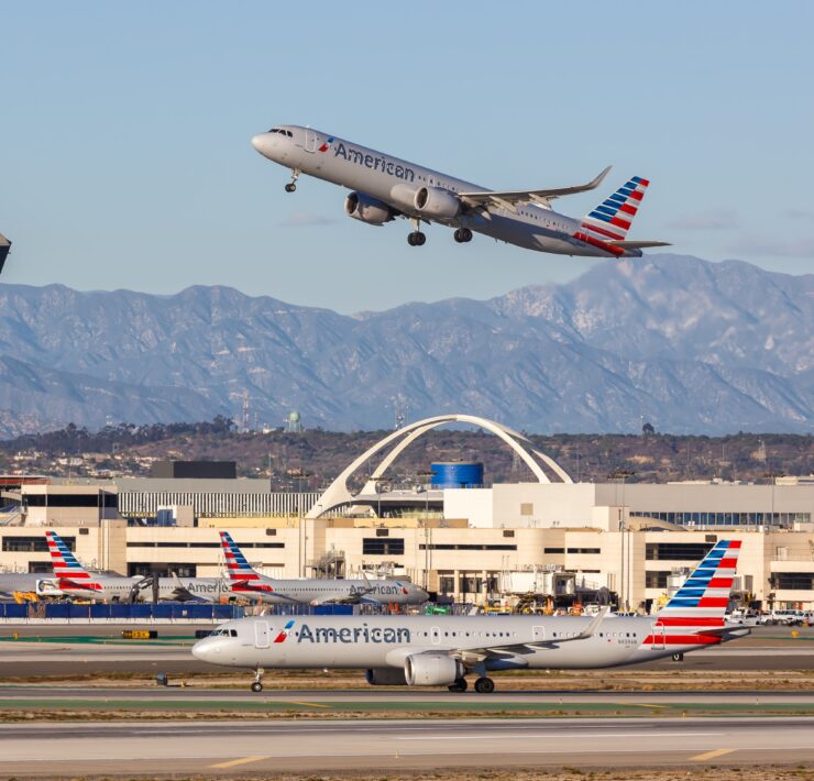 an airplane flying over a runway with buildings and mountains in the background