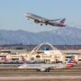 an airplane flying over a runway with buildings and mountains in the background